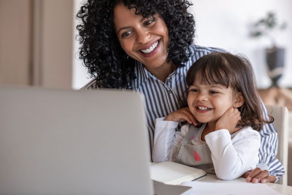 Busy mother and entrepreneur smiling while working on a laptop with her cute little girl sitting on her lap
